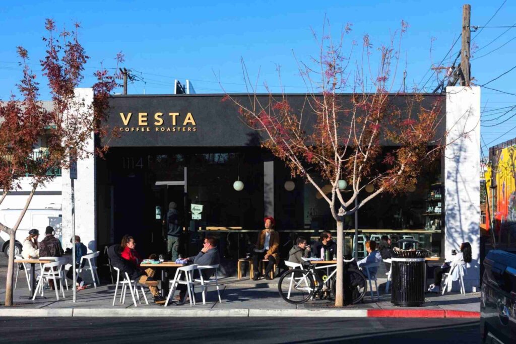 Exterior of Vesta Coffee Roasters in the Las Vegas Arts District featuring outdoor patio seating, modern black signage, and patrons enjoying coffee on a sunny day.