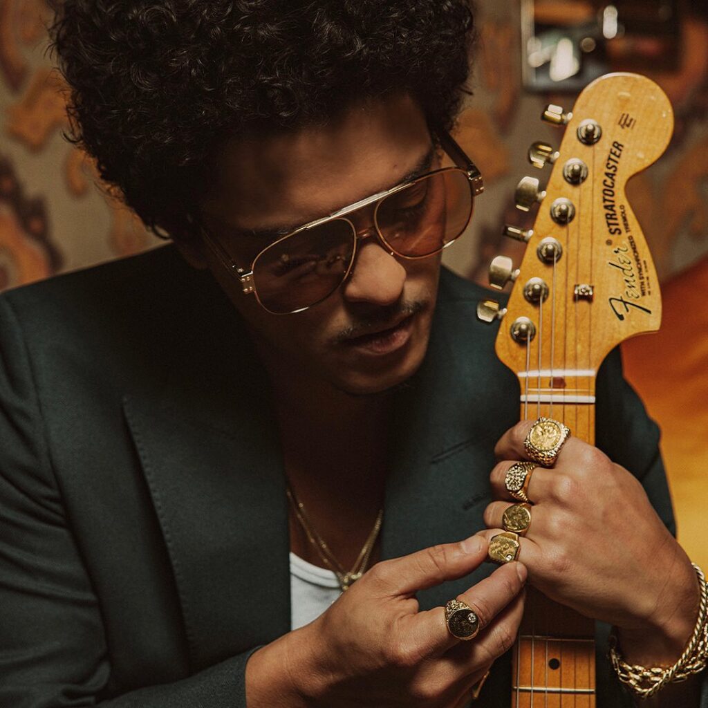 A stylish shot of Bruno Mars in a "Vegas-style" shirt and sunglasses, representing the 1970s glamour and soulful atmosphere of his Pinky Ring lounge at Bellagio.