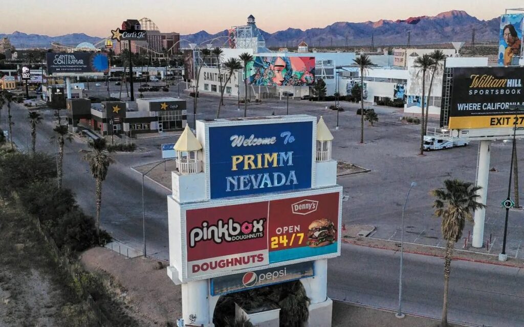 An aerial view of the Primm, Nevada skyline at sunset, showing the iconic "Welcome to Primm Nevada" sign with the Desperado roller coaster and Buffalo Bill's in the background.