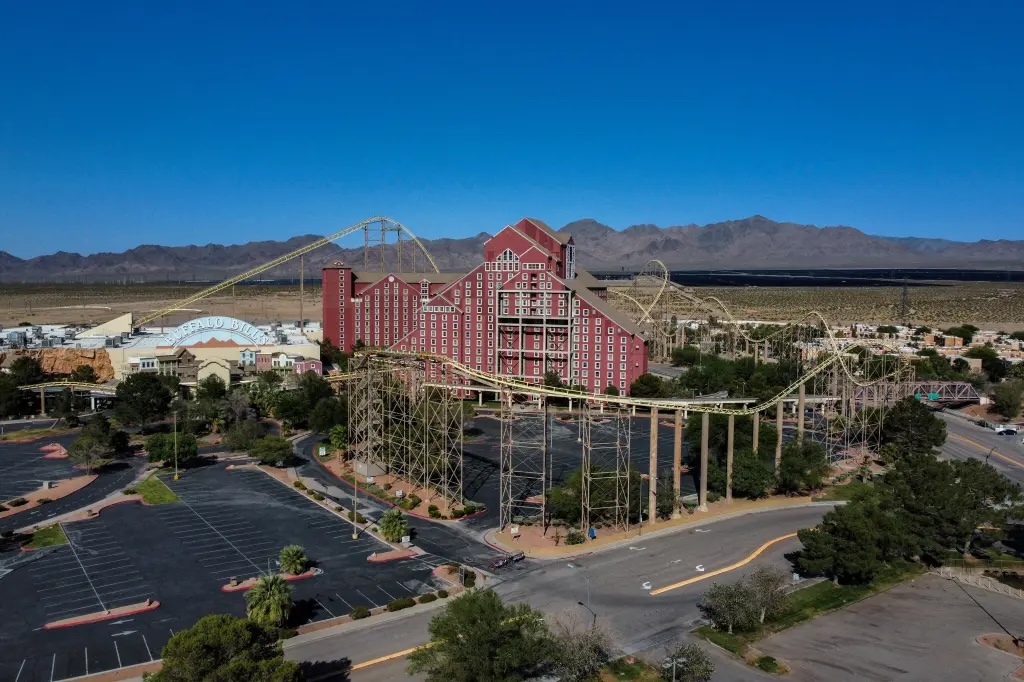 Aerial wide-angle view of Buffalo Bill's Resort and Casino in Primm, Nevada, showcasing the iconic red hotel tower and the Desperado roller coaster tracks under a clear blue sky.