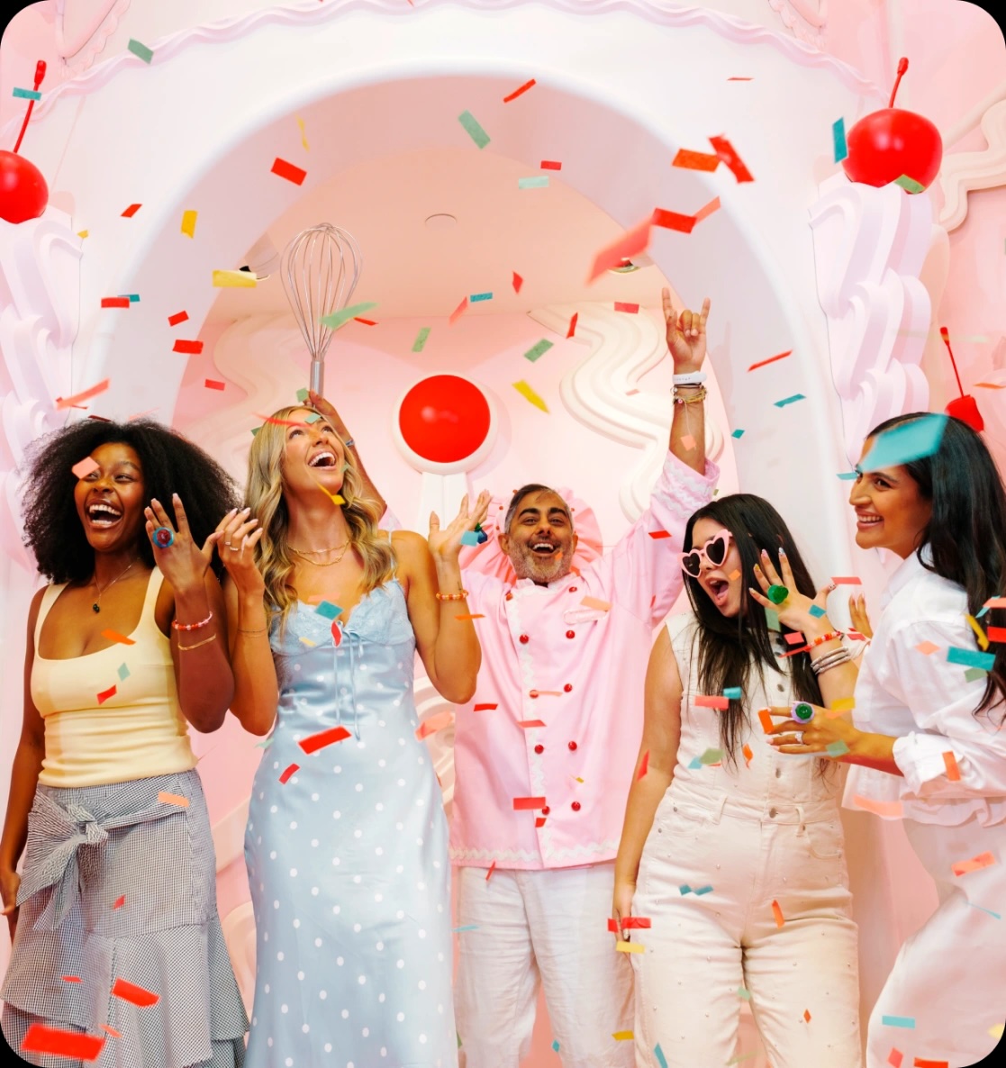 A diverse group of excited friends celebrating, laughing, and throwing colorful paper confetti under a pink archway inside the Museum of Ice Cream Las Vegas.