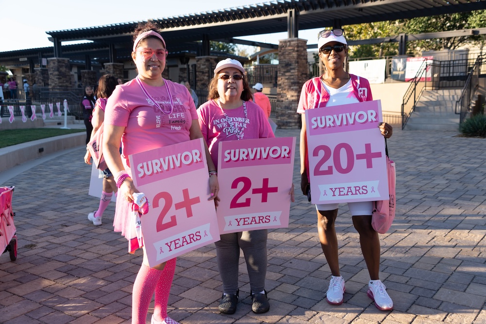 Three breast cancer survivors holding pink survivor signs at the Susan G. Komen MORE THAN PINK Walk at Town Square Las Vegas
